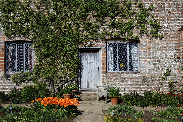 tudor cottage, old brickwork, leaded-light windows, oak door and lintel, seat, terracotta pots, daffodils