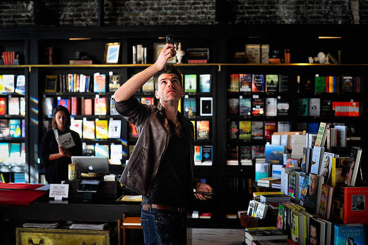 man, holding, device, near, books, store, selling