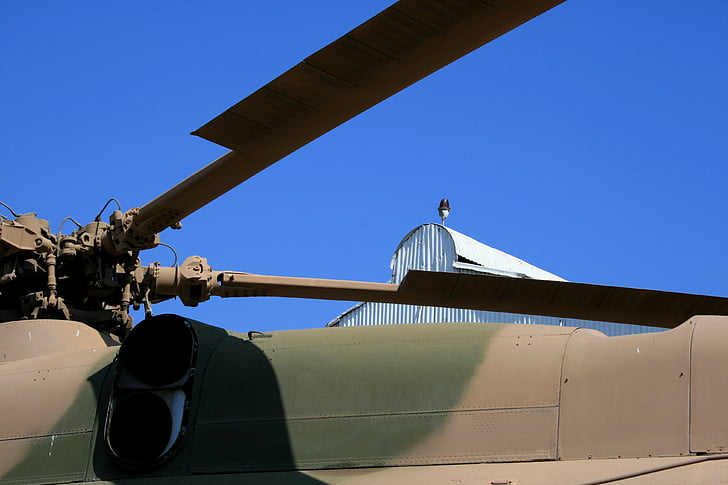 blue sky, roof of helicopter, blades of helicopter, clear sky, camouflage paint scheme, brown and green, military craft