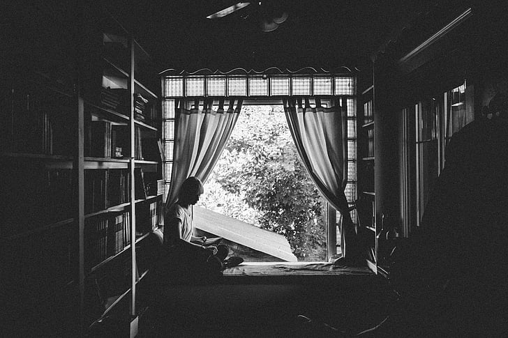 grayscale, photo, woman, reading, book, near, windows