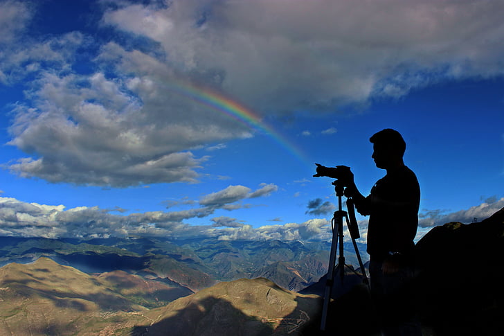 camera, clouds, mountain range, mountains, person, photographer, rainbow
