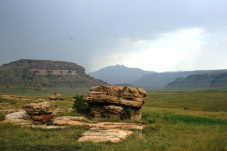 large rock, plate rocks, earthy colors, eminent storm, faroff mountains, green grass, green veld