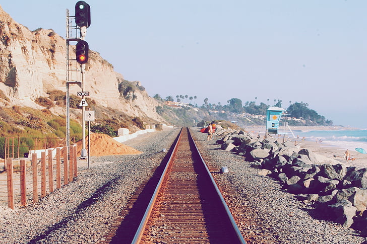 man, standing, near, sea, daytime, train tracks, pebbles