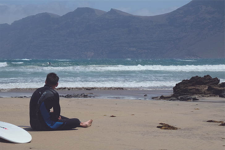 man, sitting, beach, looking, waves, daylight, surfer