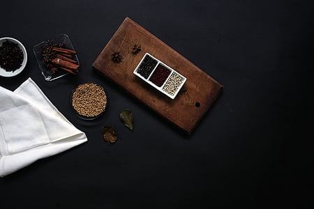 black background, container, spices, table, white cloth, wood, no people